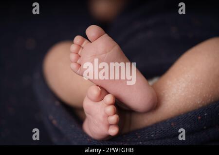 Bébé de petite taille pieds nus croisés sur une couverture bleu marine. vue rapprochée du pied de bébé le bébé est enveloppé confortablement dans une couverture bleue. nouveau-b Banque D'Images