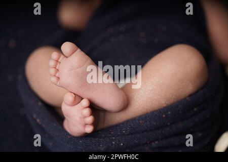 Bébé de petite taille pieds nus croisés sur une couverture bleu marine. vue rapprochée du pied de bébé le bébé est enveloppé confortablement dans une couverture bleue. nouveau-b Banque D'Images