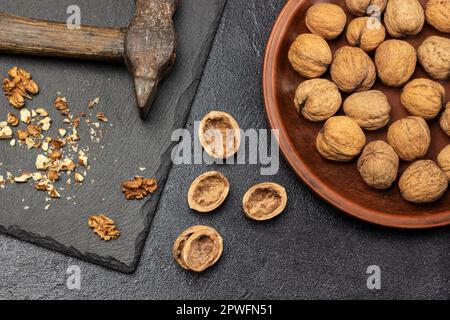 Noix écrasées et vieux marteau rouillé sur le panneau de pierre. Coque d'écrou sur la table. Écrous entiers sur plaque céramique. Pose à plat. Arrière-plan noir. Banque D'Images