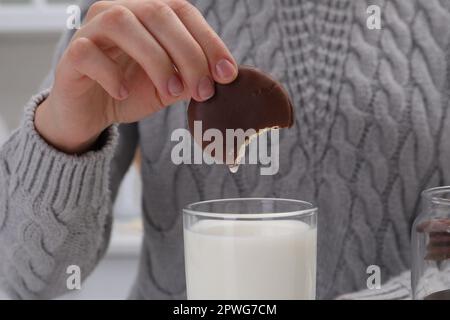 Femme trempant une délicieuse tarte au chocolat dans un verre de lait, gros plan Banque D'Images