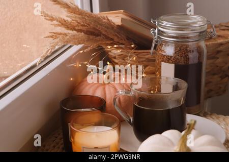 Tasse de boisson chaude, pot avec grains de café, bougies et citrouilles sur le rebord de la fenêtre à l'intérieur Banque D'Images