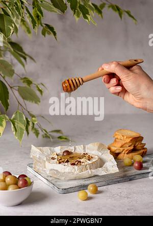 Photographie alimentaire de camembert rôti, fromage, miel, raisins, pain grillé, bruschetta, pecan, noix, pain, charcuterie, main Banque D'Images