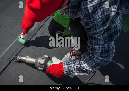 Caucasien Roofing Worker dans son 40s. Souffleur d'air chaud à l'aide de pour l'installation en caoutchouc de la membrane de toit EPDM Banque D'Images