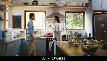 Vous êtes souriant lorsque vous vivez avec votre personne préférée. un jeune couple affectueux ayant une discussion tout en cuisinant dans sa cuisine à la maison. Banque D'Images