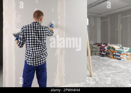 Homme plâtrage mur avec couteau à mastiquer à l'intérieur, vue arrière et espace pour le texte. Rénovation de la maison Banque D'Images