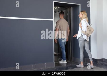 Jeune couple entrant dans l'ascenseur moderne, vue arrière Banque D'Images