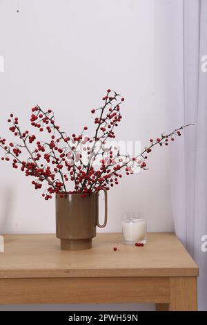 Branches de Hawthorn avec baies rouges et bougie sur table en bois à l'intérieur Banque D'Images