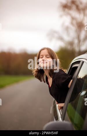 bonne fille regarde hors de la fenêtre de voiture fermer les yeux lors d'un jour d'été. Banque D'Images