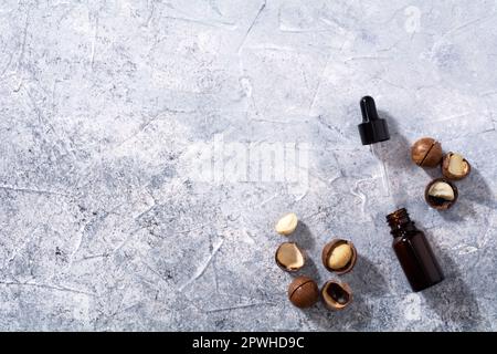 Huile de noix de macadamia naturelle dans une bouteille. Huile cosmétique. Vue de dessus noix de macadamia sur fond gris Banque D'Images