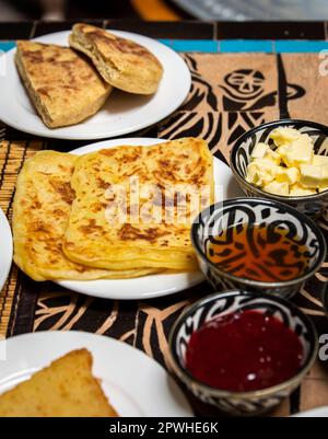 Petit-déjeuner marocain traditionnel avec crêpes, pain, beurre, miel et confiture placés sur la table à manger Banque D'Images