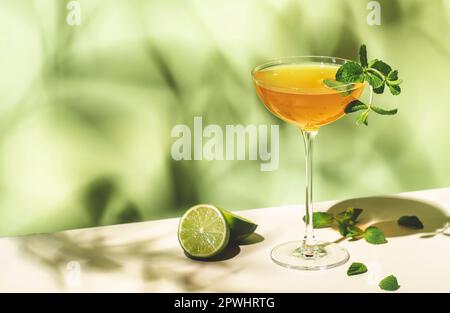 Ancienne boisson alcoolisée cubaine pour cocktail au rhum blanc, jus de lime, vin mousseux, sirop, amer, Menthe et glace. Fond vert lime, lumière dure, ombre Banque D'Images