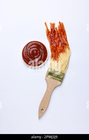 Pinceau à spaghetti trempés dans du ketchup sur fond blanc, vue de dessus. Concept créatif Banque D'Images