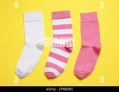 Différentes chaussettes roses et blanches sur fond jaune, plat Banque D'Images