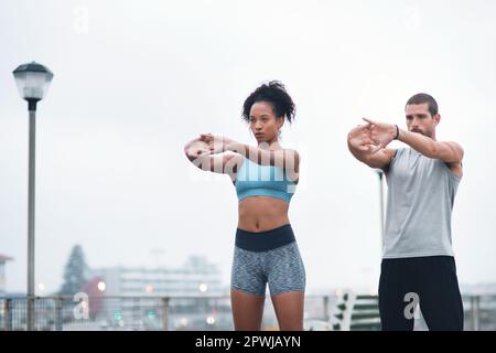 Étirez-vous aussi loin que possible à vos objectifs. deux jeunes sportifs s'étirant tout en faisant de l'exercice à l'extérieur Banque D'Images