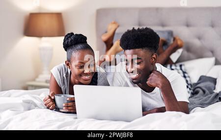 Qu'est-ce que nous allons diffuser aujourd'hui ? un jeune couple utilisant un ordinateur portable tout en se relaxant sur son lit Banque D'Images