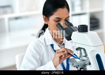 Il est temps de faire de véritables découvertes. une jeune scientifique attrayante plaçant une lame microscopique sous le microscope tout en travaillant dans un travail Banque D'Images