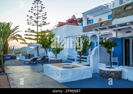 Petit hôtel typique à Mykonos, Santorin ou Crète au coucher du soleil (crépuscule). Fruit de grenade (plante en pot) avec fruits rouges et hétérophyl d'araucaria Banque D'Images