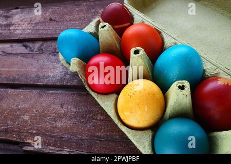 Œufs multicolores peints avec gouache et pelure d'oignon dans une boîte en carton sur fond de table en bois. Dix œufs durs. Affiche de carte postale pour Pâques. E Banque D'Images