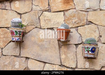 Jardinières avec cactus accrochés sur un mur en pierre. rustique, grosses pierres, argile, boue, décoration, supports métalliques, vue avant, vue avant Banque D'Images