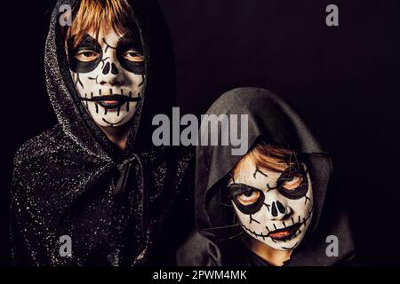 Deux enfants portent des robes sombres et de la peinture effrayante pour le visage à Halloween. Banque D'Images