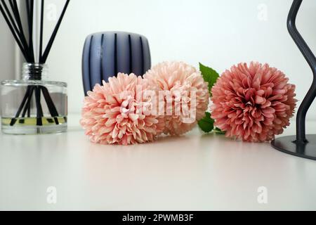 Composition avec bâtonnets d'encens, huile essentielle dans un vase en verre et fleurs artificielles en terry rose. Grand lustre en métal. Bougie parfumée à rayures grises o Banque D'Images