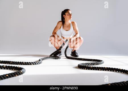 Une jeune athlète féminine s'entraîne dans une salle de sport à l'aide d'équipements de sport. FIT femme s'entraîner . Concept de fitness, de bien-être et de préparation sportive. Banque D'Images