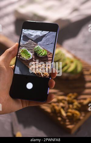 Smartphone prenant des photos à partir de sandwichs biologiques sains. Main femme. Gros plan de la table avec différents aliments. Banque D'Images