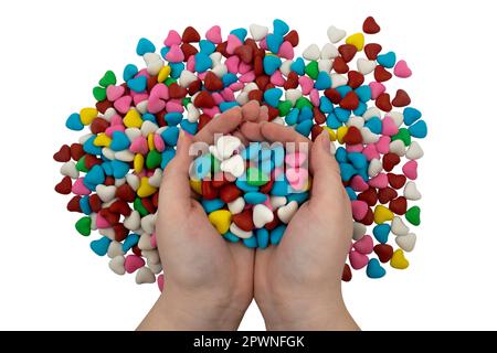 Une poignée de bonbons multicolores en forme de coeur dans les mains isolées sur un fond blanc. Gros plan, vue de dessus Banque D'Images