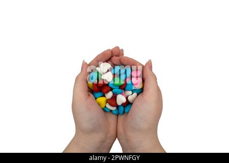 Une poignée de bonbons multicolores en forme de coeur dans les mains isolées sur un fond blanc. Gros plan, vue de dessus Banque D'Images