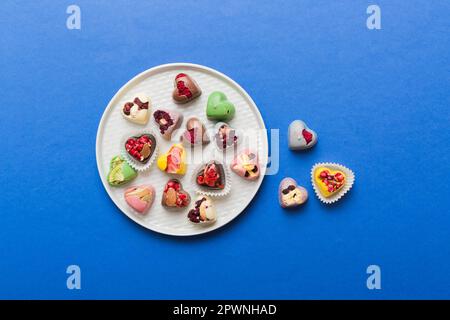 Assiette avec différents chocolats sur fond coloré. Assortiment de chocolats fins vue de dessus vith espace copie concept santé et obésité. Banque D'Images