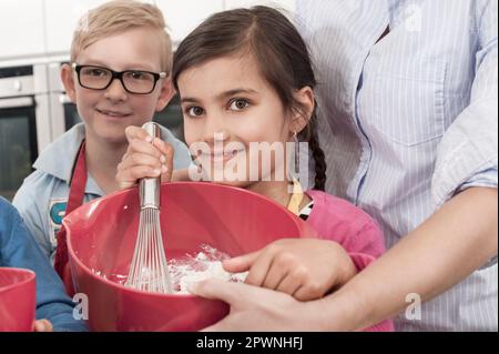 Professeur avec des étudiants battant de la crème dans un bol de mélange avec fouet en fil en classe d'économie domestique, Bavière, Allemagne Banque D'Images