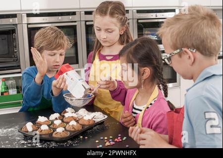 Les étudiants saupoudrent du sucre en poudre sur les muffins de la classe d'économie domestique, Bavière, Allemagne Banque D'Images