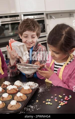 Les étudiants saupoudrent du sucre en poudre sur les muffins de la classe d'économie domestique, Bavière, Allemagne Banque D'Images