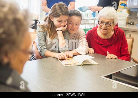 Les femmes âgées avec des filles lisant le livre au repos à la maison Banque D'Images