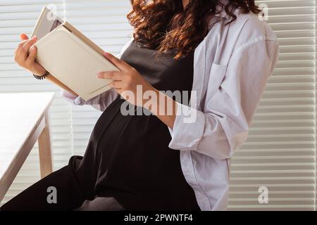 Gros plan de la femme enceinte lisant le livre à la maison. Concept matin et grossesse. Banque D'Images