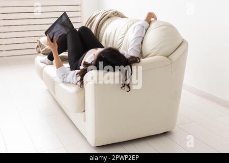 Femme enceinte latine utilisant un ordinateur tablette assis sur un canapé à la maison. Grossesse et information pour la parentalité Banque D'Images