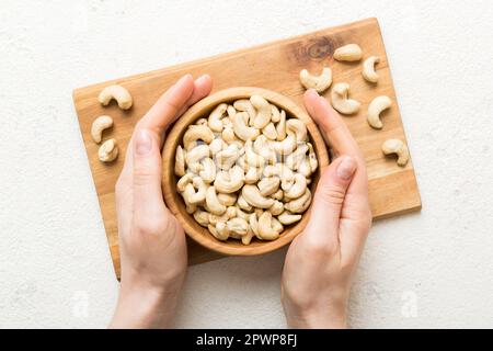 Femme mains tenant un bol en bois avec noix de cajou. Aliments sains et en-cas. En-cas végétariens de différentes noix. Banque D'Images