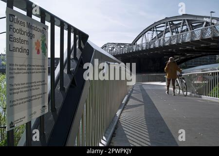 une femme pousse un vélo sur la passerelle des prés de dukes, sous le pont barnes sur la tamise, chiswick, londres, angleterre, avec un avis du conseil à côté Banque D'Images