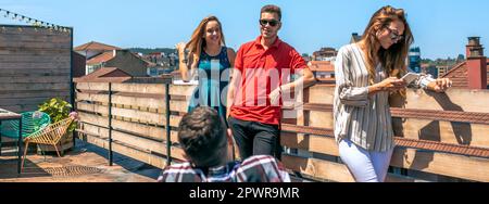 Des amis heureux parlant dans la ville sur le toit alors qu'une femme regarde son téléphone Banque D'Images