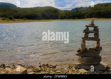 Pyramide des pierres sur la plage contre les montagnes et le lac. Concept de spiritualité, détente, zen. Banque D'Images