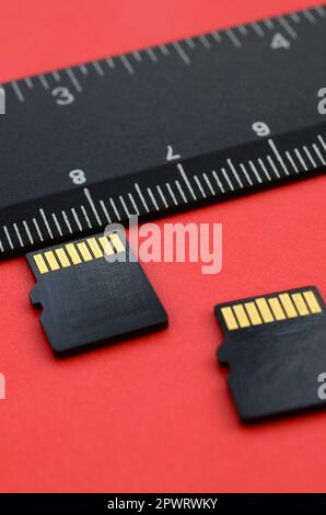 Deux petites cartes mémoire micro SD se trouvent sur un arrière-plan rouge à côté d'une règle noire. Un petit magasin de données et d'informations compact Banque D'Images
