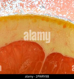 Vue rapprochée de la tranche de pamplemousse rouge sur fond d'eau. Texture de la boisson fraîche aux fruits avec macro bulles sur la paroi en verre. Conception plate. Banque D'Images