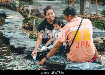 KANCHANABURI -THAÏLANDE, 30 MARS 2023 : touristes non identifiés viennent visiter et nourrir koi ou carpe fantaisie dans un petit étang avec beau jardin décoré Banque D'Images