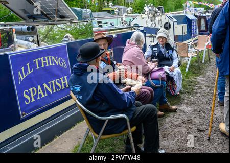 Groupe de personnes, certains en costume d'époque, assis sur un sentier de remorquage boueux sur un canal en dégustant une tasse de thé avec des amis. Banque D'Images