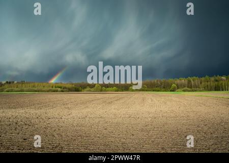 Des nuages fantastiques avec un arc-en-ciel et un champ labouré, vue sur la campagne printanière Banque D'Images