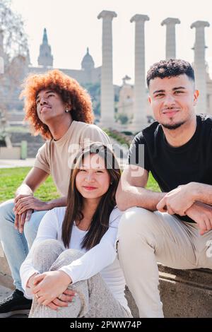 Portrait vertical d'un groupe de jeunes multiraciaux assis à l'extérieur ensemble. Les adolescents souriant regardant l'appareil photo. Une femme asiatique avec ses amis. Divers étudiants se liant à une réunion sociale. Photo de haute qualité Banque D'Images