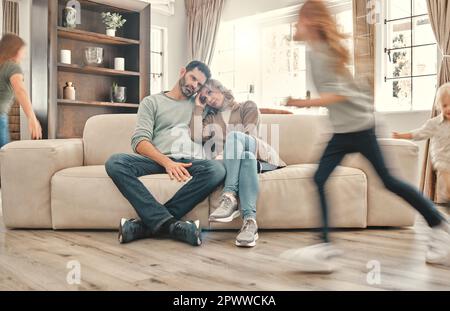 La maison est de plus en plus petite de jour. deux parents épuisés sur le canapé pendant que les enfants jouent à la maison Banque D'Images