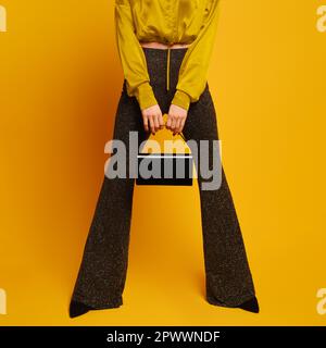 Les jambes des femmes dans un pantalon évasé sont écartées et les mains tiennent un sac entre elles sur fond jaune studio Banque D'Images