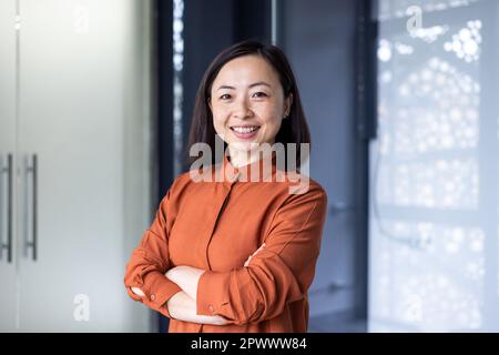 Portrait d'une jeune femme d'affaires asiatique belle et prospère, d'une employée souriante et regardant un appareil photo aux bras croisés, d'une femme financière satisfaite des résultats de son travail. Banque D'Images