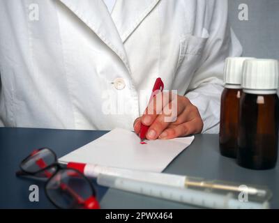 Un médecin gaucher écrit quelque chose sur le papier. Stylo pour écrire à la main. Une blouse blanche est portée par un professionnel de la santé. Mains d'un médecin ou Banque D'Images